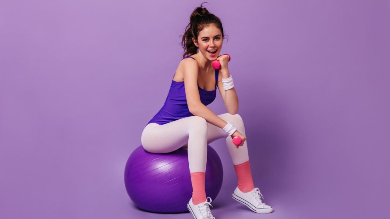 Active fitness trainer woman in tights in style of 80s demonstrates exercise for hands on fit ball.