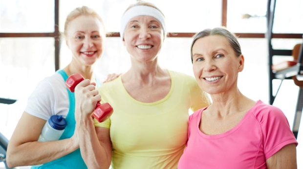 Happy mature women with toothy smiles looking at you during training in sports center