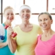 Happy mature women with toothy smiles looking at you during training in sports center